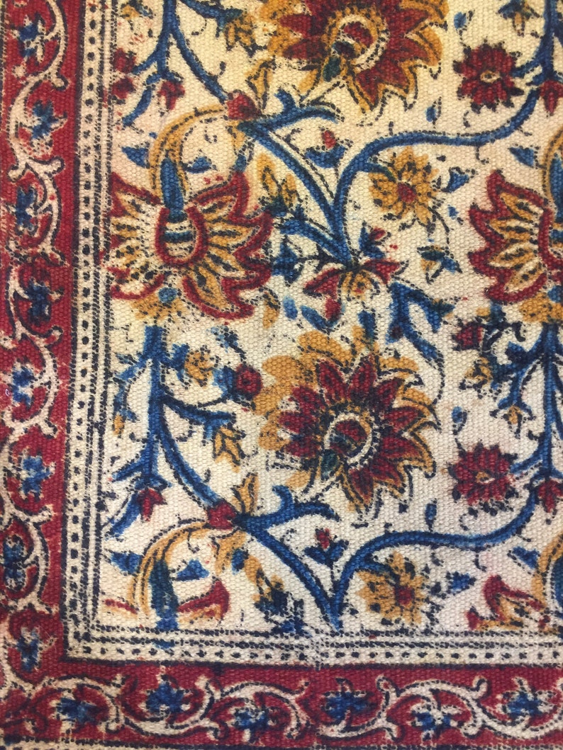 May include: A close-up of a fabric with a floral pattern. The fabric is white with blue, red, and yellow flowers. The fabric has a border of red and blue.