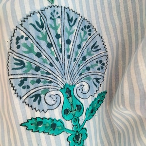May include: A blue and green floral design on a white and blue striped fabric. The design features a large, stylized flower with a fan-like shape and intricate details.
