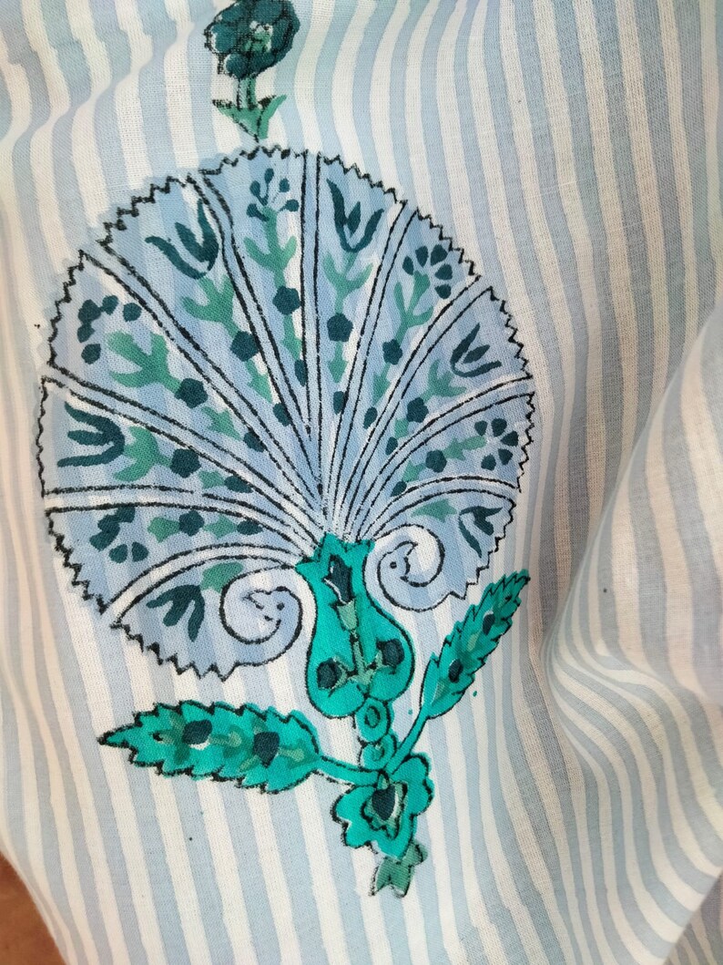 May include: A blue and green floral design on a white and blue striped fabric. The design features a large, stylized flower with a fan-like shape and intricate details.