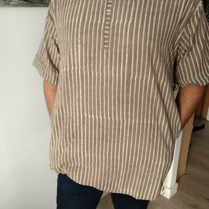 May include: A brown and white striped shirt with a short sleeve and a v-neck. The shirt has a button closure at the neck.
