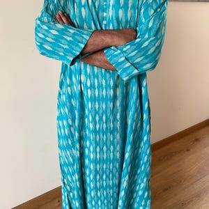 May include: A long turquoise blue tunic with a white geometric pattern. The tunic has a button-up front and long sleeves.