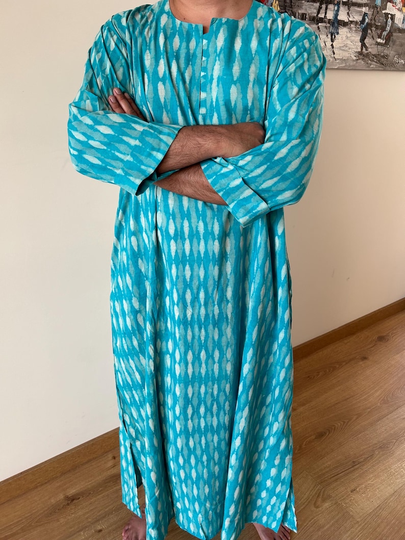 May include: A long turquoise blue tunic with a white geometric pattern. The tunic has a button-up front and long sleeves.