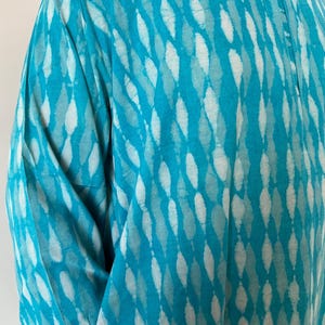 May include: A turquoise blue shirt with a white and turquoise pattern. The shirt has a button-up collar and a short sleeve.