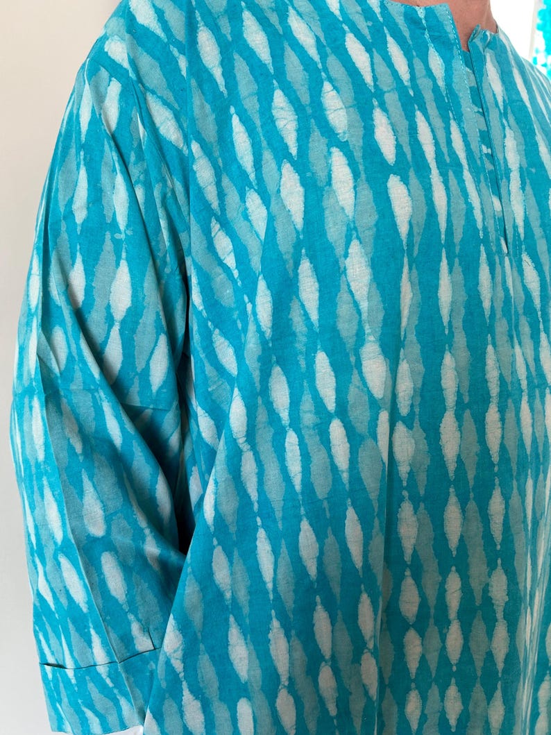 May include: A turquoise blue shirt with a white and turquoise pattern. The shirt has a button-up collar and a short sleeve.