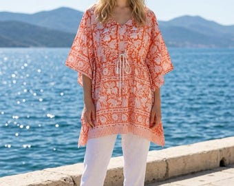 May include: An orange and white floral print tunic with a V-neckline, short kimono-style sleeves, and a drawstring waist, paired with plain white trousers and simple white flat sandals. The tunic features a repeating botanical pattern throughout.