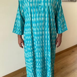 May include: A turquoise blue long-sleeved shirt with a white and turquoise pattern. The shirt has a button-up collar and a relaxed fit.