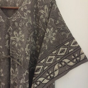 May include: A gray cotton kaftan with a floral print and a geometric border. The kaftan has a V-neck and a tie at the waist.