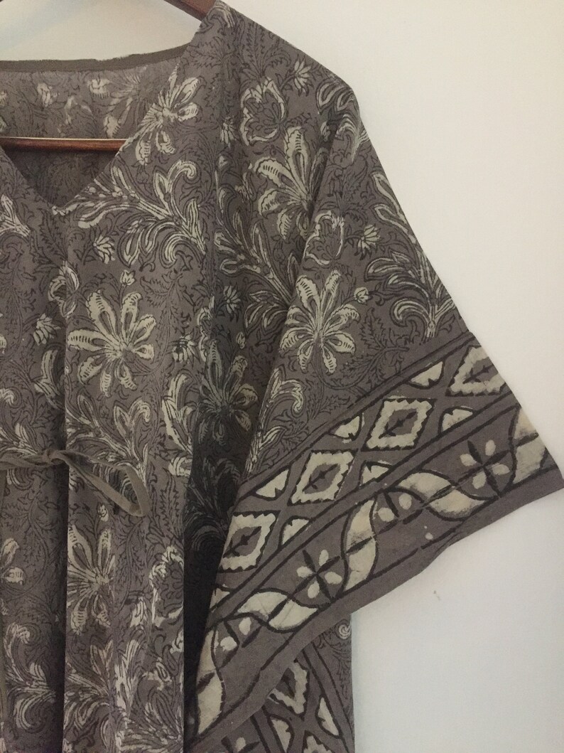 May include: A gray cotton kaftan with a floral print and a geometric border. The kaftan has a V-neck and a tie at the waist.