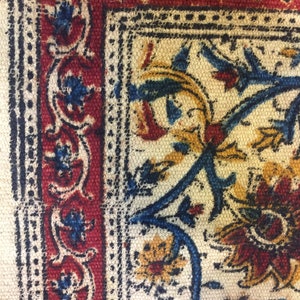 May include: Close-up of a fabric with a repeating pattern of blue, red, and yellow floral designs. The fabric has a white background and a textured surface.