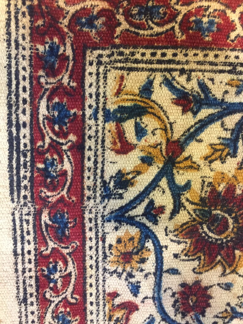 May include: Close-up of a fabric with a repeating pattern of blue, red, and yellow floral designs. The fabric has a white background and a textured surface.