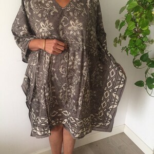 May include: A gray and white floral print kaftan with a geometric border. The kaftan has a V-neck and 3/4 sleeves.