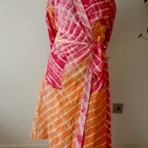 May include: A pink and orange tie-dye robe with a long, flowing design. The robe has a wrap closure and a belt.