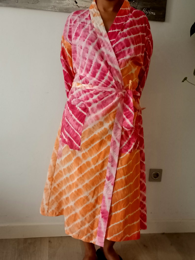 May include: A pink and orange tie-dye robe with a long, flowing design. The robe has a wrap closure and a belt.