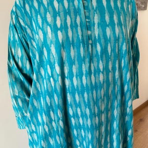 May include: A turquoise blue tunic with a white diamond pattern. The tunic has a round neckline and three-quarter sleeves.