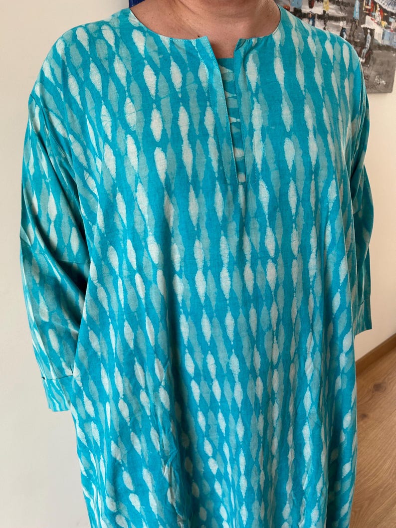 May include: A turquoise blue tunic with a white diamond pattern. The tunic has a round neckline and three-quarter sleeves.