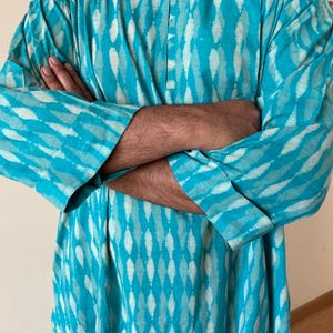 May include: A turquoise blue long-sleeved shirt with a white and turquoise pattern. The shirt has a button-up collar and a relaxed fit.