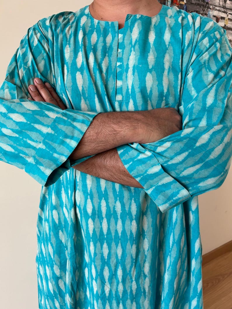 May include: A turquoise blue long-sleeved shirt with a white and turquoise pattern. The shirt has a button-up collar and a relaxed fit.
