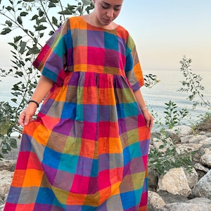 May include: A colorful, plaid-patterned dress in shades of orange, pink, purple, green, and blue. The dress features a round neckline, short sleeves, and a gathered waist. The long, flowing skirt falls to the ankles. The dress is made of a lightweight fabric, perfect for warm weather.