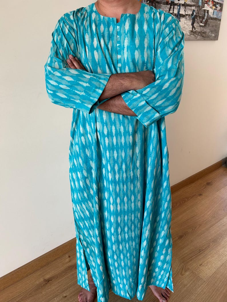 May include: A long, turquoise blue tunic with a white geometric pattern. The tunic has a button-up neckline and long sleeves.