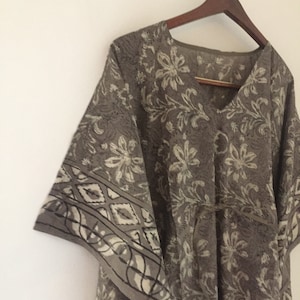May include: A gray and white floral print kaftan with a V-neck and a tie belt. The kaftan has a loose, flowing fit and is perfect for warm weather.