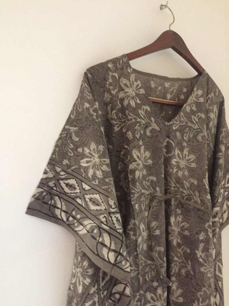 May include: A gray and white floral print kaftan with a V-neck and a tie belt. The kaftan has a loose, flowing fit and is perfect for warm weather.