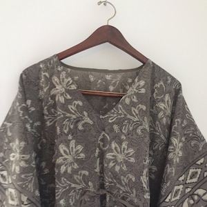 May include: A gray and white floral print kaftan with a V-neck and a tie at the waist.