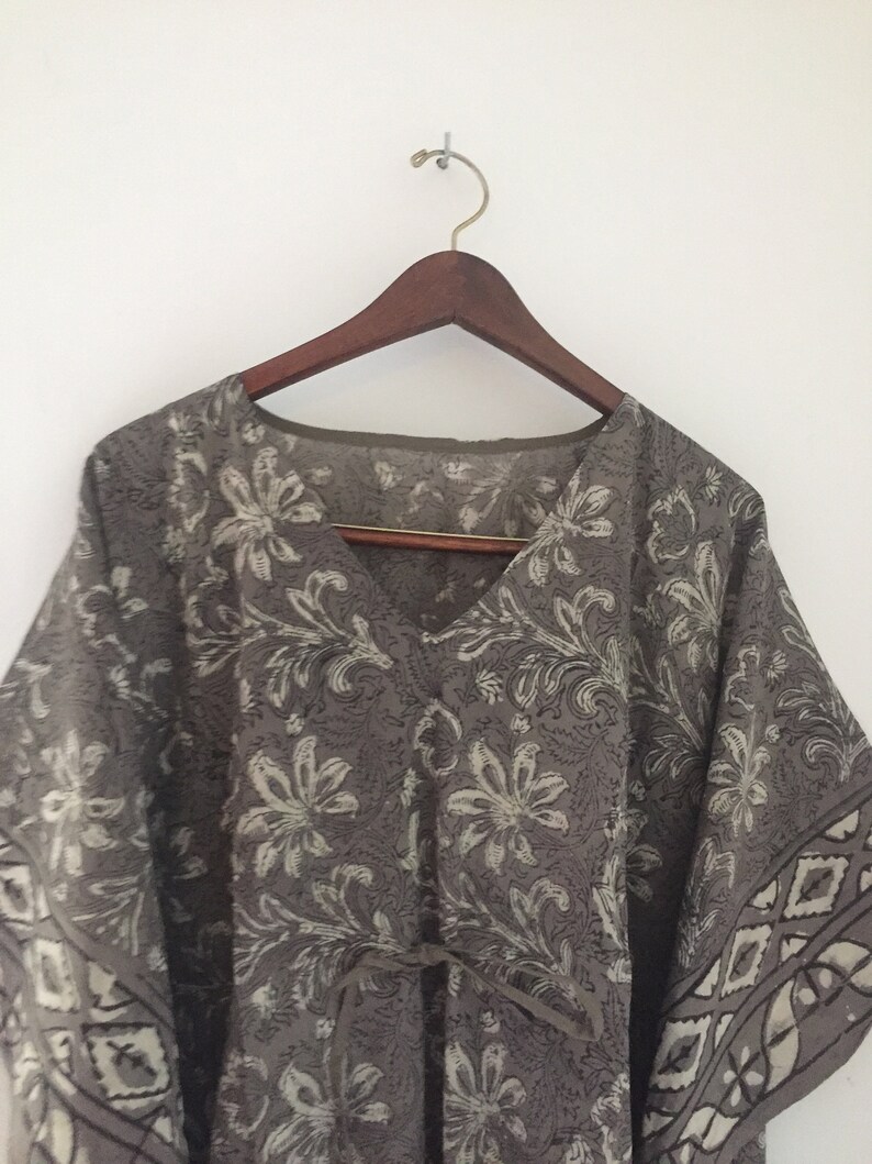 May include: A gray and white floral print kaftan with a V-neck and a tie at the waist.