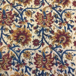 May include: A white fabric with a repeating pattern of blue, red, and yellow floral designs. The fabric has a textured surface.
