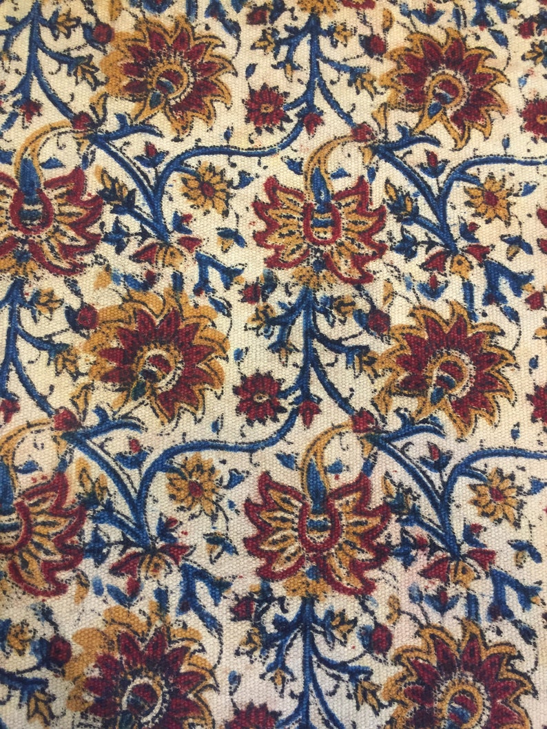 May include: A white fabric with a repeating pattern of blue, red, and yellow floral designs. The fabric has a textured surface.
