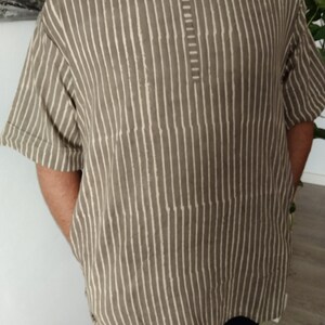 May include: A striped, short-sleeved shirt with a V-neck and a button closure. The shirt is made of a light brown fabric with white stripes.