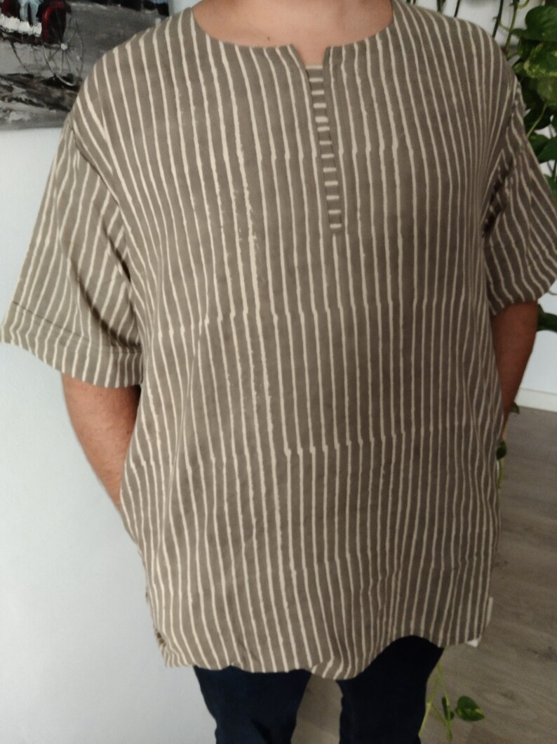May include: A striped, short-sleeved shirt with a V-neck and a button closure. The shirt is made of a light brown fabric with white stripes.