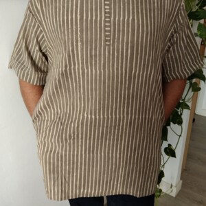 May include: A brown and white striped shirt with a short sleeve and a v-neck.