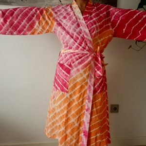 May include: A pink and orange tie-dye robe with a long sleeve and a wrap closure. The robe has a pocket on the left side.