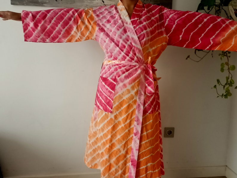 May include: A pink and orange tie-dye robe with a long sleeve and a wrap closure. The robe has a pocket on the left side.