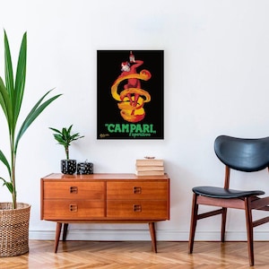 Puede incluir: Un póster vintage enmarcado de Campari Aperitivo. La obra de arte presenta una figura roja sosteniendo una botella, con un diseño en espiral amarillo y naranja sobre un fondo negro. El texto "CAMPARI, Aperitivo" es verde.