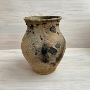 以下が含まれることがあります： 口が広く丸みを帯びた、素朴な茶色の粘土製の壺。壺は、黒と茶色の模様がついた、使い込まれたアンティークな外観をしています。