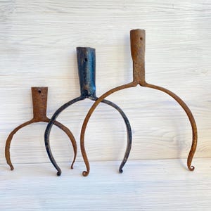 May include: Three metal tools with cylindrical sockets and curved, fork-like prongs. The smallest tool is rusted brown, the middle tool is dark grey with a smooth finish, and the largest tool is heavily rusted brown. Each has a small hole.