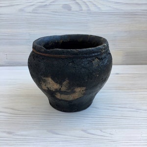 May include: Black ceramic pot with a rustic, textured finish. The pot has a wide, round opening and a slightly flared base.