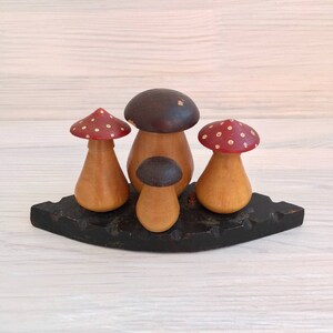 May include: Set of four wooden mushroom shaped salt and pepper shakers. The shakers are painted in red, brown, and white. The shakers are arranged on a black wooden base.