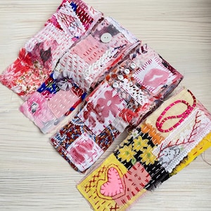Può includere: Una collezione di polsini in tessuto patchwork colorato. I polsini presentano vari motivi, tra cui stampe floreali, cuori e la parola "LOVE" scritta con piccole perline. Ogni polsino è cucito a mano con filo visibile e adornato con bottoni e pizzo.