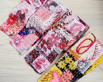 Könnte beinhalten: Eine Sammlung bunter Patchwork-Stoff-Armbänder. Die Armbänder weisen verschiedene Muster auf, darunter Blumenmuster, Herzen und das Wort "LOVE", das mit kleinen Perlen geschrieben wurde. Jedes Armband ist handgenäht mit sichtbarem Faden und mit Knöpfen und Spitze verziert.