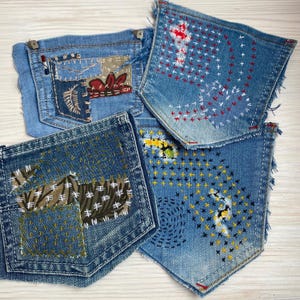 May include: Four detached denim pockets featuring various embroidery styles. One pocket has a brown patch with white stitching, another displays red and white cross-stitch patterns, a third shows yellow and black cross-stitching, and the fourth has a brown patterned fabric patch with white embroidery.