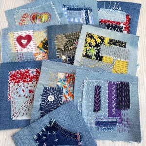 May include: A collection of denim fabric squares, each uniquely embellished with colorful patches and decorative stitching. Some squares feature heart and floral designs, while others showcase geometric patterns and button accents. The patchwork style creates a handcrafted aesthetic.