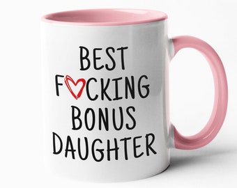 Puede incluir: Taza de cerámica blanca con borde y asa de color rosa. La taza tiene texto negro que dice "BEST F♥CKING BONUS DAUGHTER".