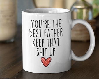 Puede incluir: Taza de café de cerámica blanca con texto negro que dice "You're the best father keep that shit up" con un corazón rojo.