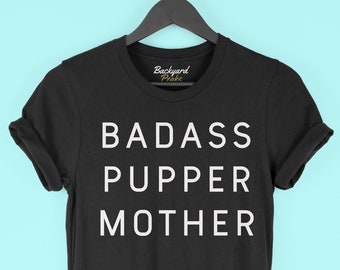 May include: Black t-shirt with white text that reads "BADASS PUPPER MOTHER".