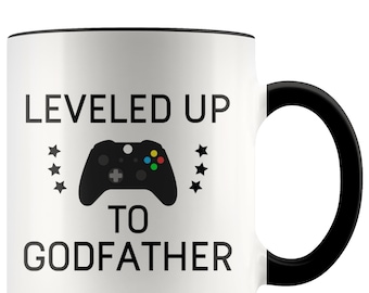 May include: White ceramic mug with a black handle and rim. The mug features the text "LEVELED UP TO GODFATHER" with a black controller graphic and star accents. A fun gift for gamers.