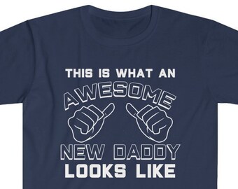 May include: Navy blue t-shirt with white text that reads "This is what an awesome new daddy looks like". The text is surrounded by two white thumbs up symbols.