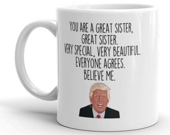 May include: White ceramic mug with a black handle. The mug features a black and white image of a man with a red tie and the text "YOU ARE A GREAT SISTER, GREAT SISTER. VERY SPECIAL, VERY BEAUTIFUL. EVERYONE AGREES. BELIEVE ME."
