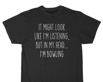 May include: Black t-shirt with the white text: "IT MIGHT LOOK LIKE I'M LISTENING, BUT IN MY HEAD... I'M BOWLING." The shirt has short sleeves and a crew neck. The fabric appears to be a soft, comfortable material.